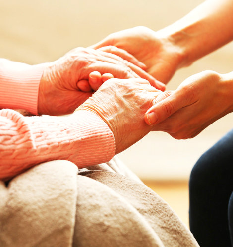 senior woman's hand holding caregiver's hands