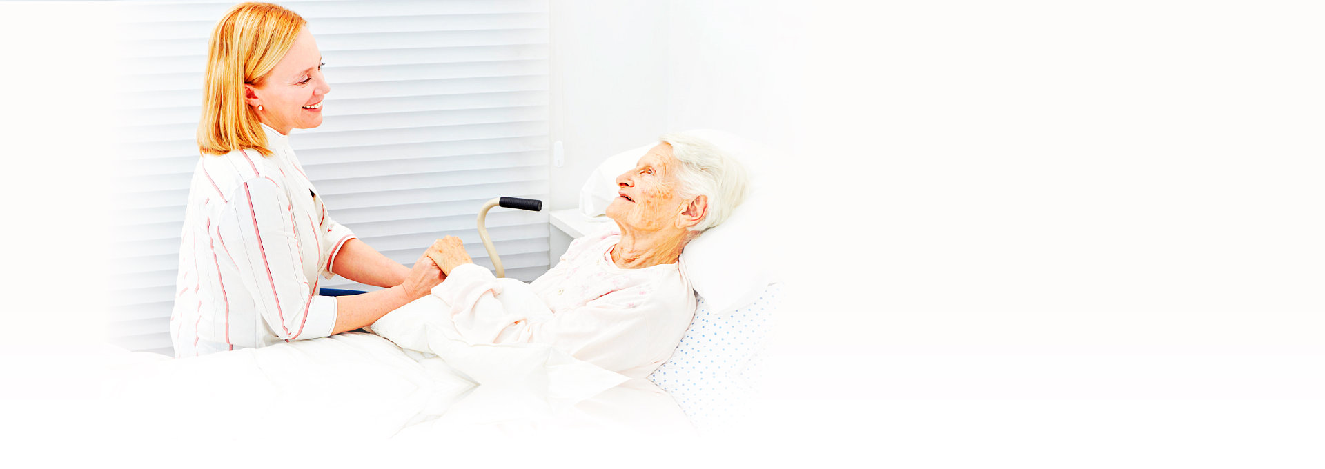 senior woman lying in bed talking to her caregiver
